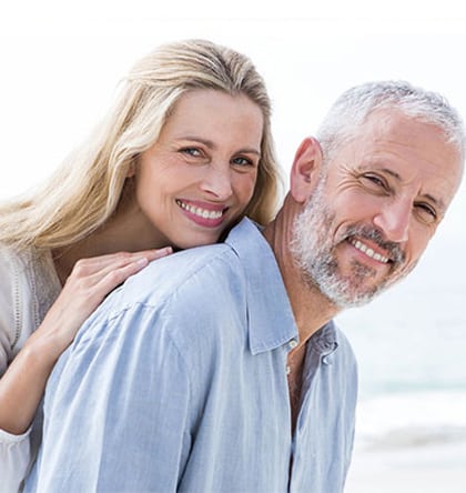 Head and shoulders photo of middle-aged couple smiling at the beach, for information on dental implants from Kentucky Dental Group of Lexington.